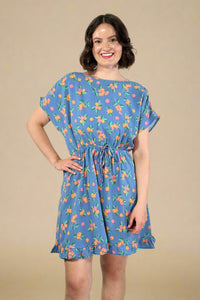 Woman wearing a short sleeve blue floral dress with elastic waist against a plain background