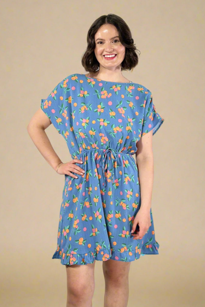 Woman wearing a short sleeve blue floral dress with elastic waist against a plain background