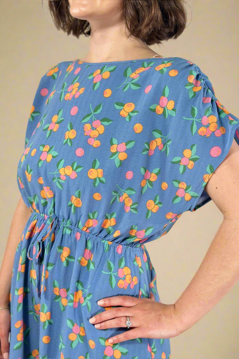 Woman wearing a blue dress with colorful fruit pattern against a plain background