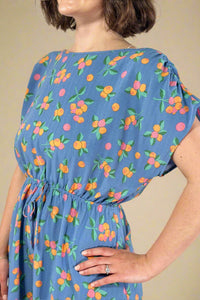 Woman wearing a blue dress with colorful fruit pattern against a plain background