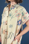 Beige shirt with floral patterns worn by a person on a plain background