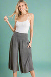 A pair of women’s lightweight dark heather grey gaucho pants falling just below the knees and featuring soft, flowy material, elastic waistband, and pockets. 