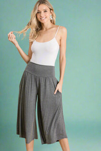 A pair of women’s lightweight dark heather grey gaucho pants falling just below the knees and featuring soft, flowy material, elastic waistband, and pockets. 