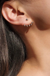 Silver ear jacket style earrings featuring one small ball in the front with a row of five balls that peak out from under your lobe. 