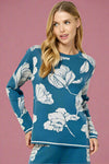 Knit blue sweater featuring a bold white floral jacquard print. Long sleeve, full length, with a crew neckline. 