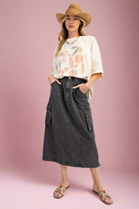 A women’s midi length, a-line,  elastic waisted cargo pocket skirt in a soft faded black denim.