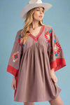 A womens short babydoll style v neck dress in mocha with red side panels and sleeve ends featuring bright embroidery along neckline, chest, and wide sleeves and 100% cotton material.
