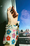 An image of a wrist wrap pouch in a multi colored daisy pattern with zip closures. Made from recycled, plastic free materials.