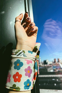 An image of a wrist wrap pouch in a multi colored daisy pattern with zip closures. Made from recycled, plastic free materials.