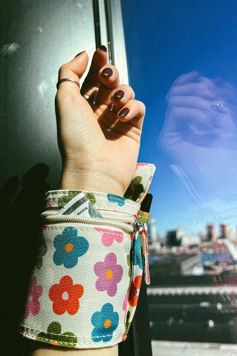 An image of a wrist wrap pouch in a multi colored daisy pattern with zip closures. Made from recycled, plastic free materials.