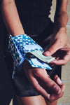 An image of a wrist wrap pouch in a blue daisy pattern with Velcro closures. Made from recycled, plastic free materials.