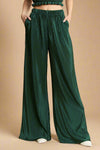 Model is wearing high waisted wide leg pants made from a shimmery green plisse fabric. 