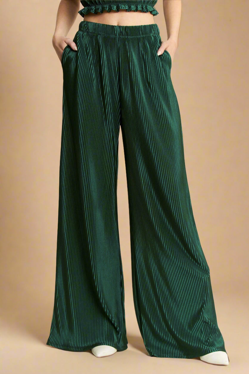 Model is wearing high waisted wide leg pants made from a shimmery green plisse fabric. 