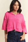 Model is wearing a soft bright pink cropped sweater that features short drop shoulder sleeves and a relaxed polo collar. 
