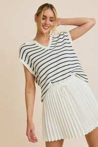 Model is wearing a drop shoulder collared v neck sleeveless sweater top with blue and white stripes.