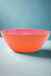 A large melamine serving bowl that is bright orange on the outside and hot pink on the inside.