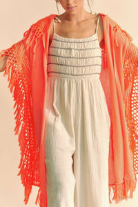 Model is wearing a bright orange lightweight knit fringed edge poncho.