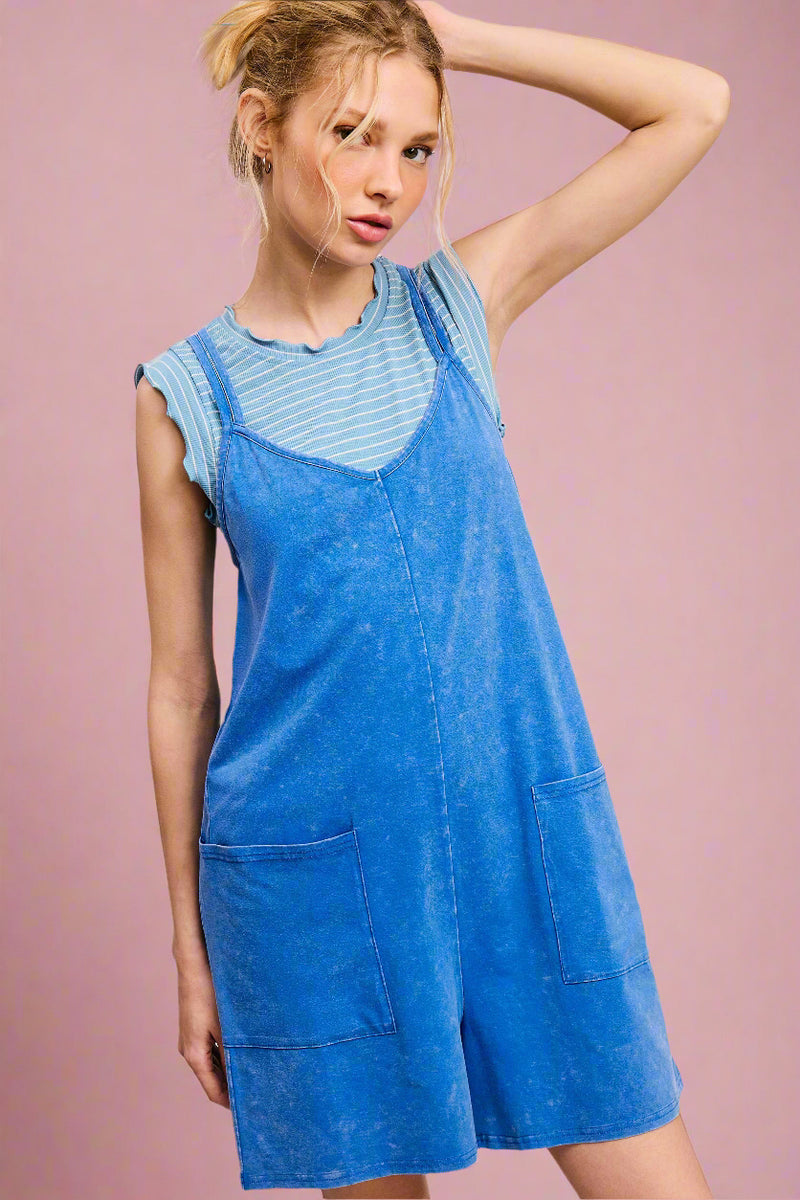 Woman wearing a blue denim pinafore dress over a striped shirt on a light pink background