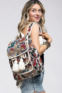 Handmade embellished flap backpack with an outside pocket, adjustable straps, tassels, and a vibrant paisley pattern.