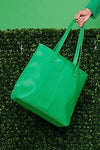 A green, vegan leather tote bag with zipper closures.