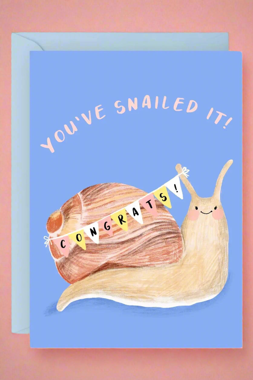 A light blue greeting card with an image of a snail with a pennant banner across it reading ‘Congrats!’ and text that reads ‘You’ve Snailed It!’ across the top.