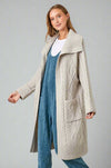 A women’s heavy weight cable knit long cardigan featuring oversized fit, long sleeves, front pockets, and shawl collar in a light taupe.