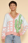 Model is wearing a colorful cardigan that features a bright cactus and geometric pattern. 