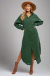 Woman wearing a green dress with a slit, brown boots, and a beige hat on a white background