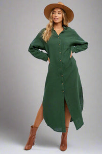 Woman wearing a green dress with a slit, brown boots, and a beige hat on a white background