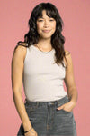 Woman wearing a beige tank top and gray jeans against a white background