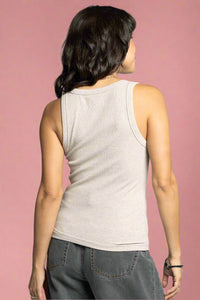 Woman wearing a beige tank top and gray pants on a plain background