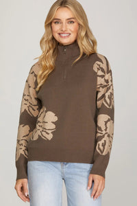 Woman wearing a brown sweater with beige floral patterns on sleeves against a plain background