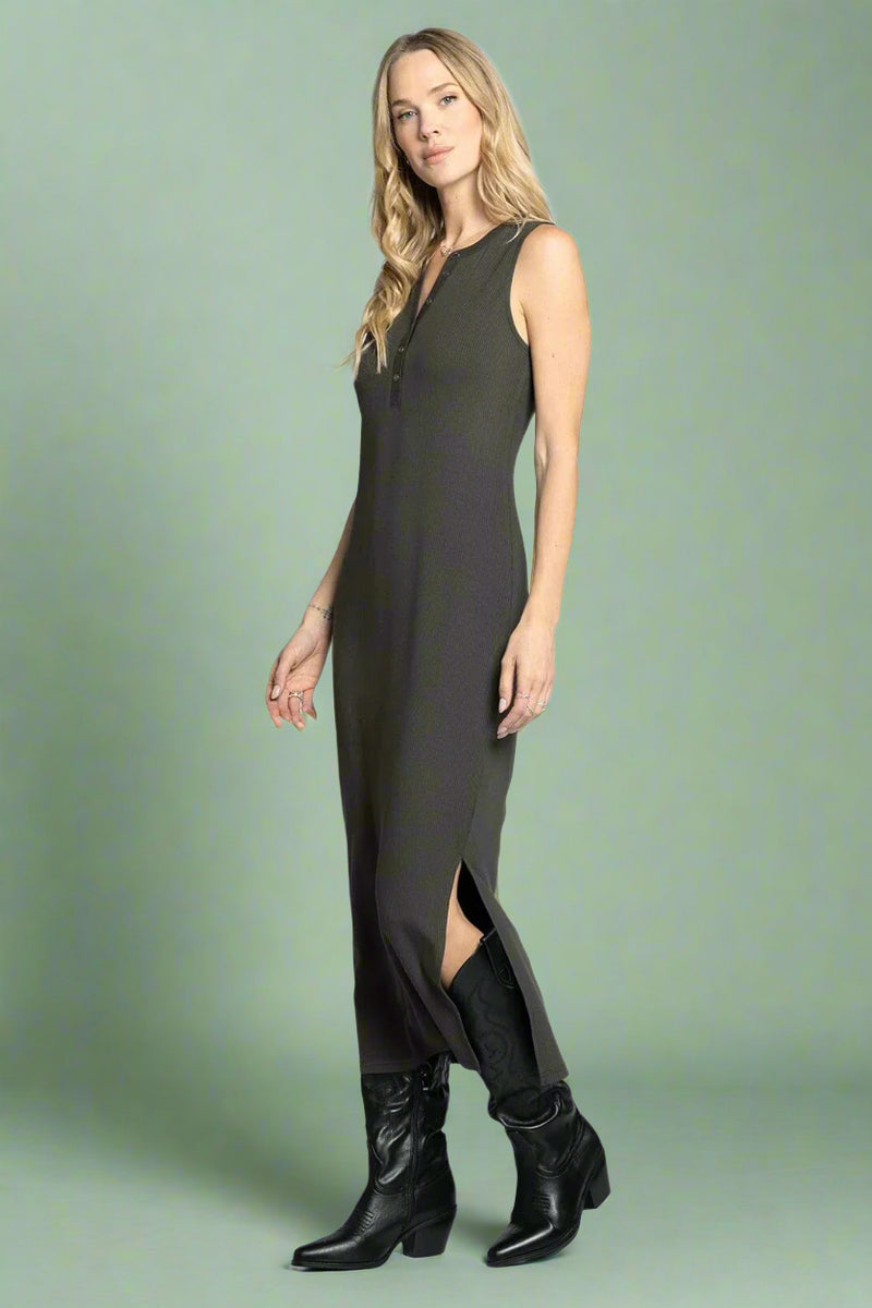 Woman wearing a sleeveless green dress with a slit and black boots on a white background