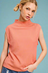 Model is wearing a lightweight high neck, cap sleeve blouse in a peach color.