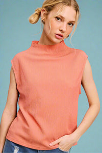 Model is wearing a lightweight high neck, cap sleeve blouse in a peach color.