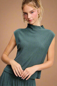 Model is wearing a high neck, cap sleeve blouse in dark teal.