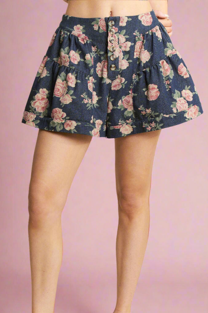 Model is wearing dark denim colored shorts that feature a pink rose print with a high waist and exposed button fly.