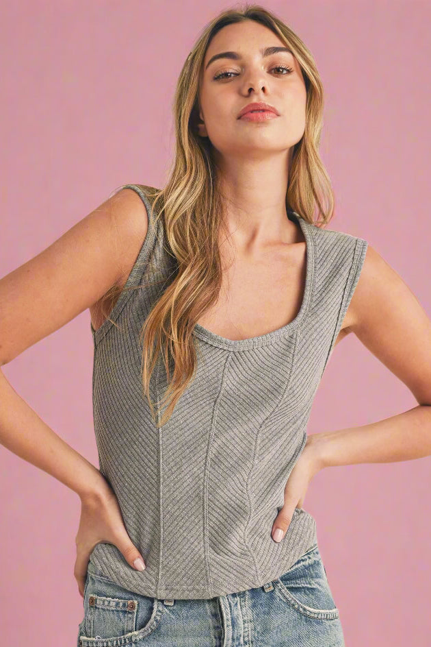 Model is wearing a flattering square neck tank top in heather gray. Tank features wide straps and alternating diagonal ribbed panels. 