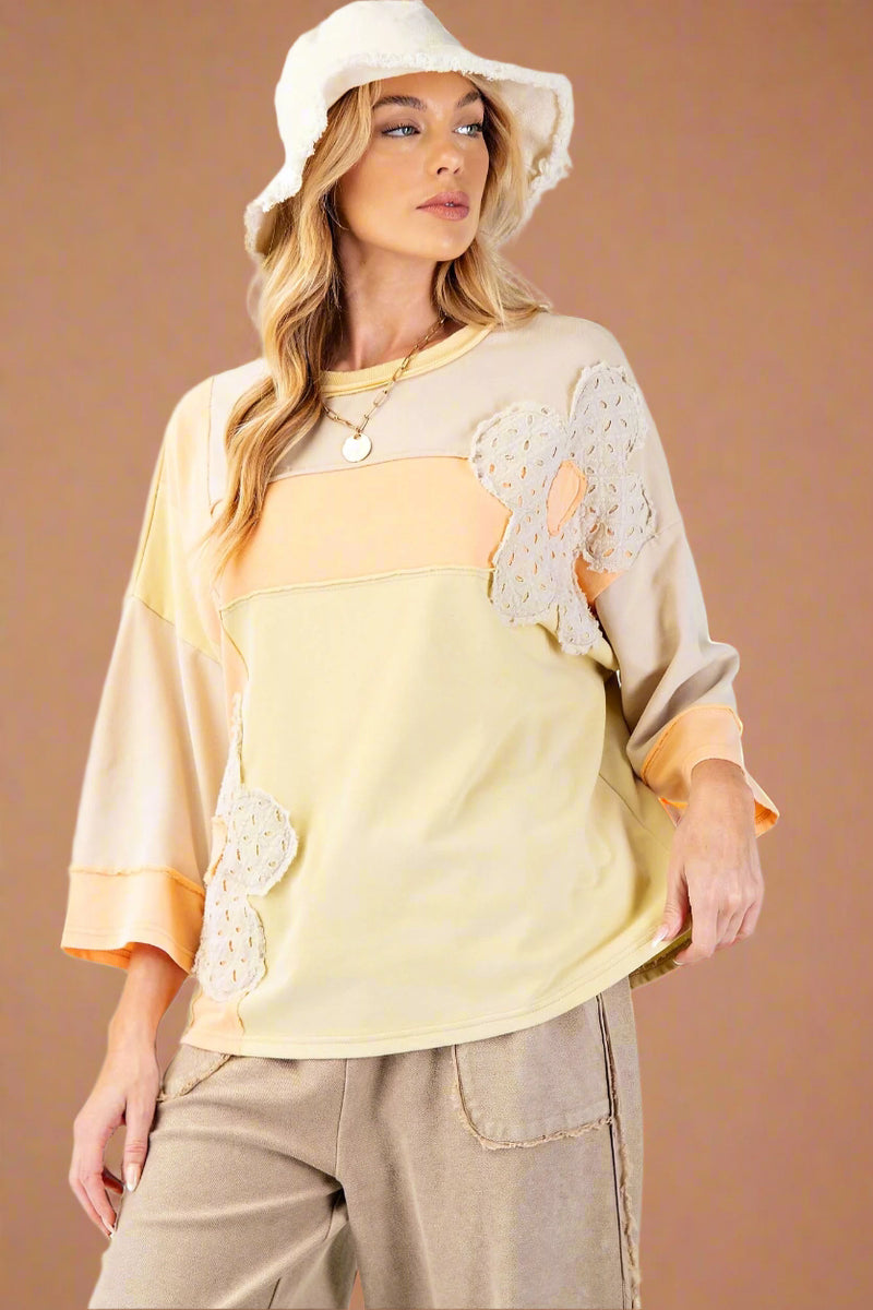 Model is wearing an oversized boho style patchwork top with dolman sleeves and flower embellishments. 