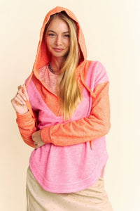 Model is wearing a two-toned heathered v neck hoodie with a hi-lo dolphin hem in bright orange and pink.