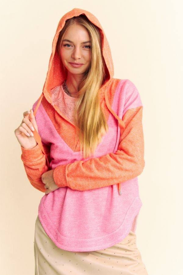 Model is wearing a two-toned heathered v neck hoodie with a hi-lo dolphin hem in bright orange and pink.