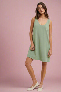 Model is wearing a sage green colored tank shift dress with two white stripes on the side and pockets. 