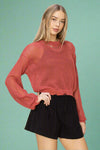Model is wearing a loose knit cropped rust colored sweater featuring distressed detailing on the cuffs and along with hem. 