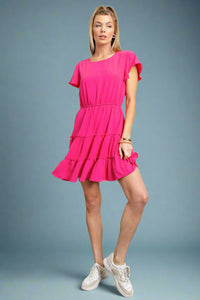 A short sleeve scoop neck mini dress in hot pink with elastic waistband and tiered ruffle skirt.