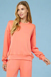 Model is wearing a bright coral colored crew neck sweatshirt in a buttery soft material.