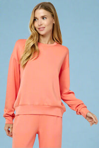 Model is wearing a bright coral colored crew neck sweatshirt in a buttery soft material.