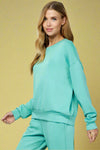 Model is wearing a turquoise colored soft crew neck long sleeve sweatshirt. 
