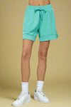Model is wearing mid length buttery soft turquoise colored shorts with an adjustable tie waist and pockets. 