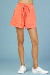 Model is wearing high rise mid length buttery soft shorts in a vibrant coral color. 