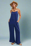 A wide leg jumpsuit in blue. It has adjustable spaghetti straps and a ruffle detail neckline.